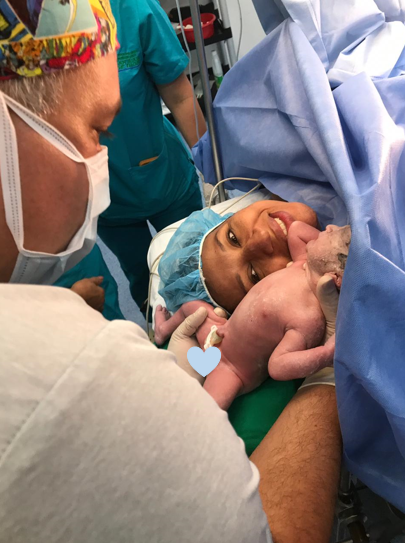 Madre conociendo a su bebé recién nacido en sala de cirugía, acompañada por el equipo médico durante la adaptación neonatal.